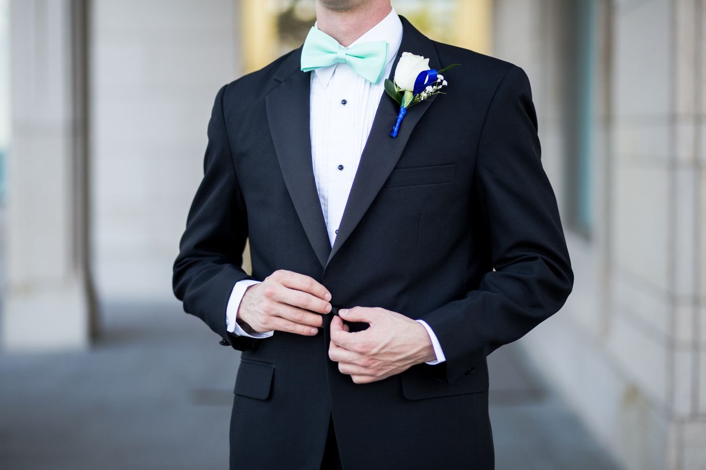 Representative photo of a groom in a black tuxedo fastening the jacket button