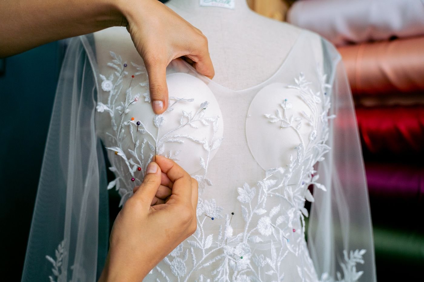 Representative photo of hands pinning lace on a white wedding gown fitted to a dress form
