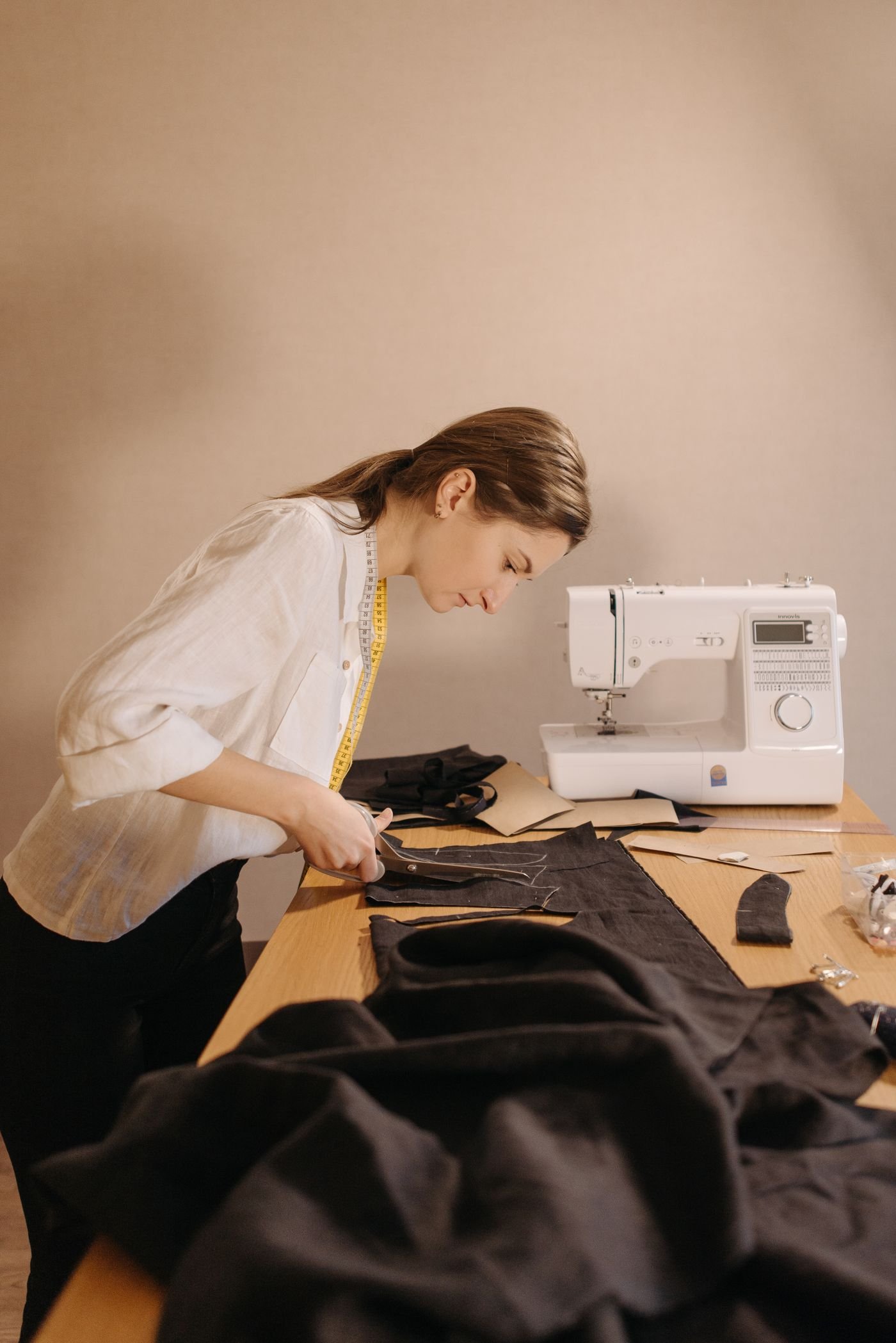 Representative photo of a tailor cutting fabric from a pattern at a workbench beside a sewing machine