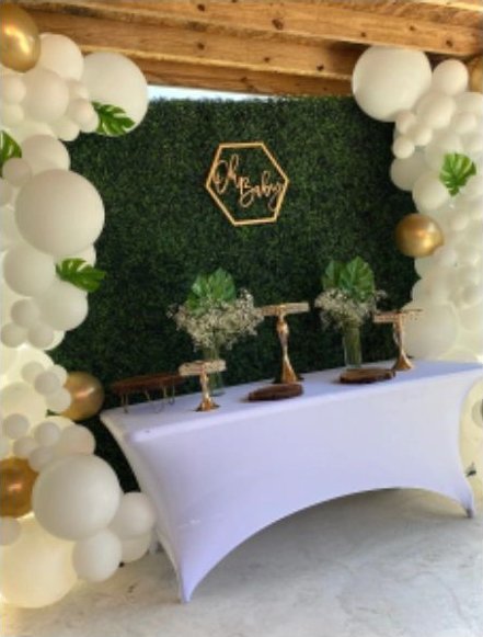 Representative photo of a cream and gold balloon arch framing a boxwood backdrop and a styled main table