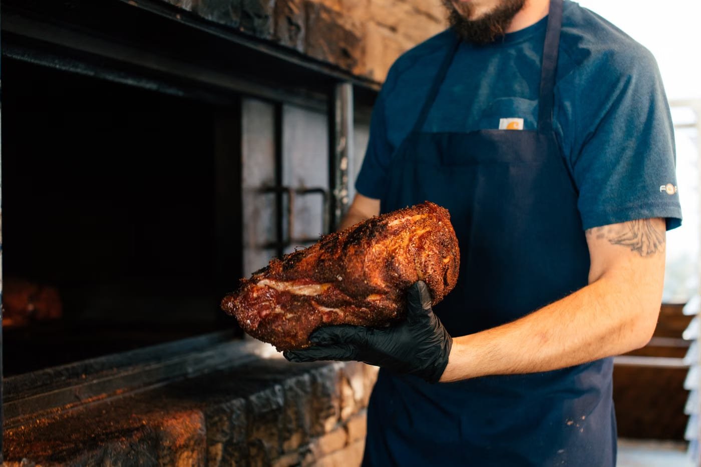 Pitmaster pulling a smoked brisket from a brick wood-fired smoker at Boss Bully BBQ