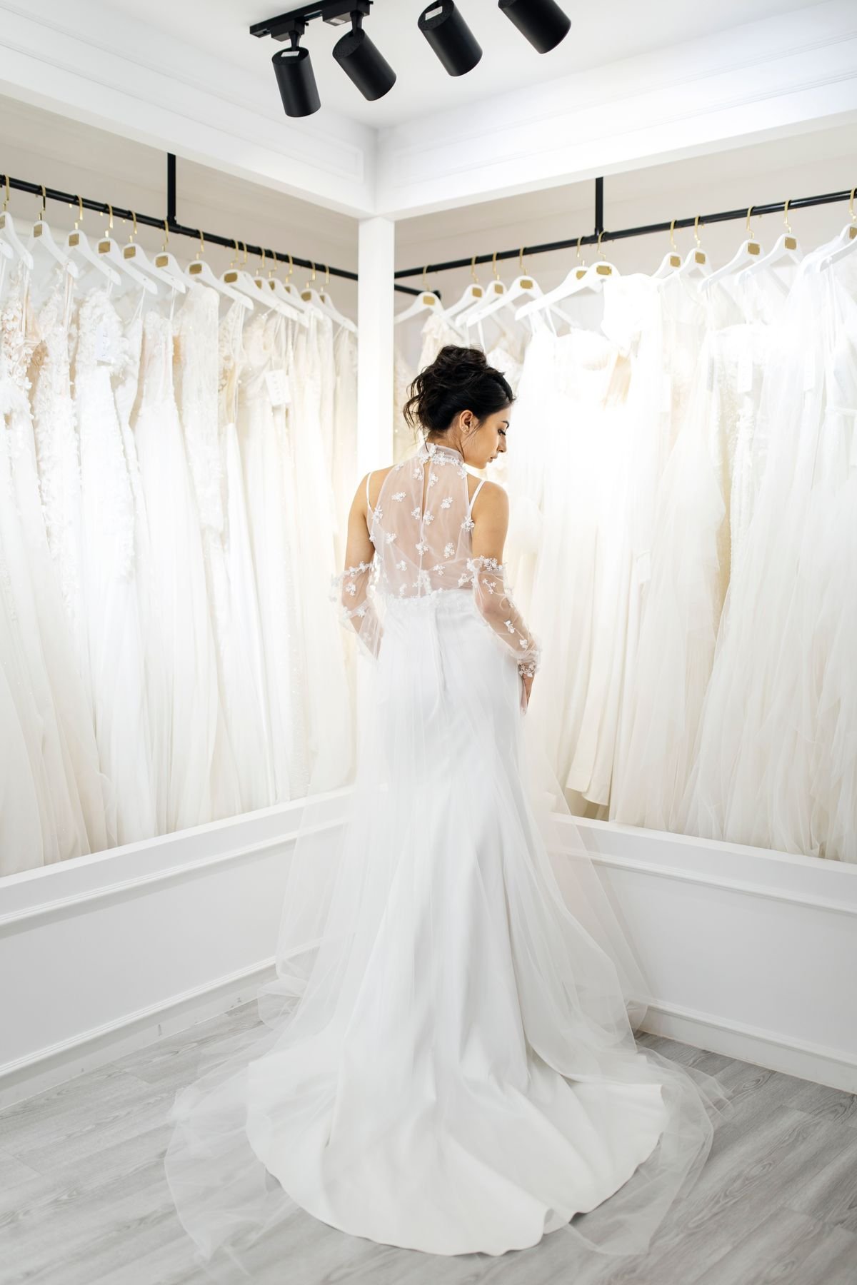 A bride in a fitted lace-and-tulle gown in a bridal boutique lined with wedding dresses &mdash; representative photo.