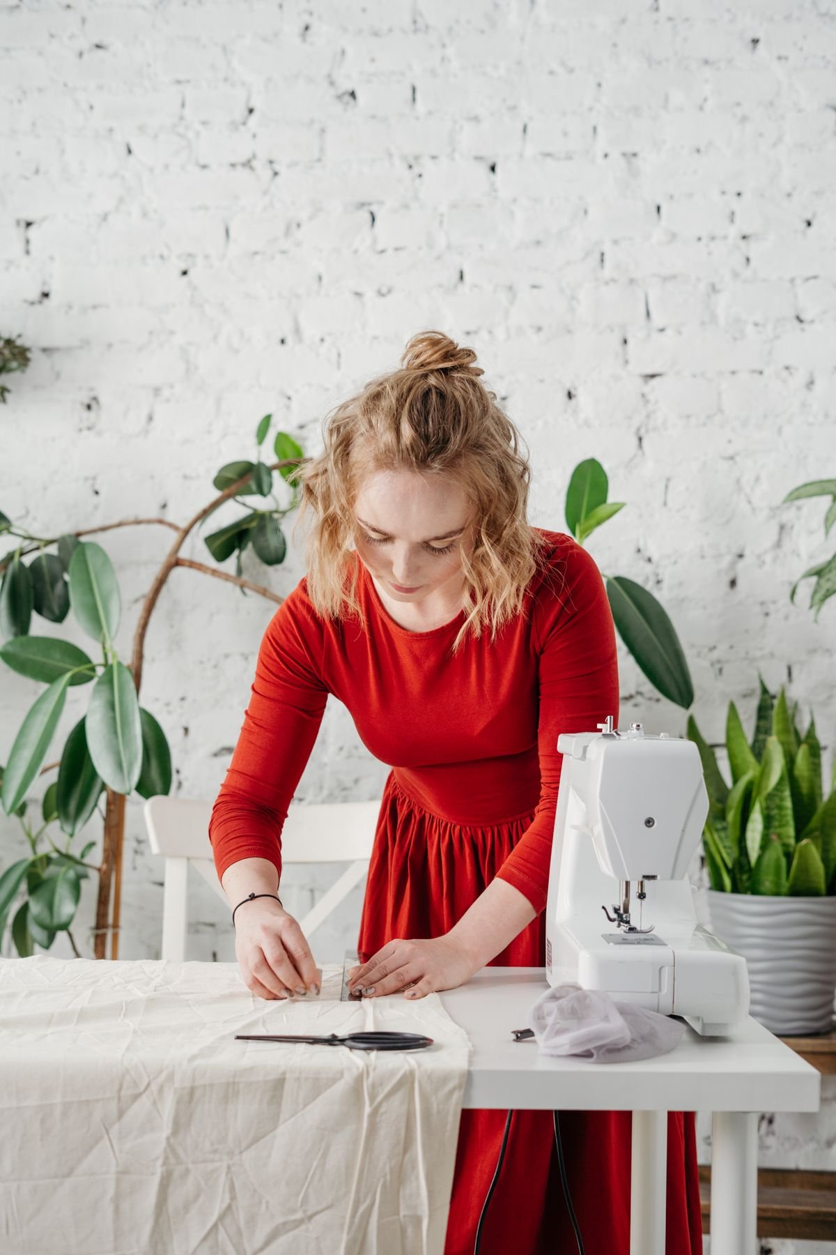 A seamstress marking and pinning fabric at a sewing table in a bright studio &mdash; representative photo of alteration work.