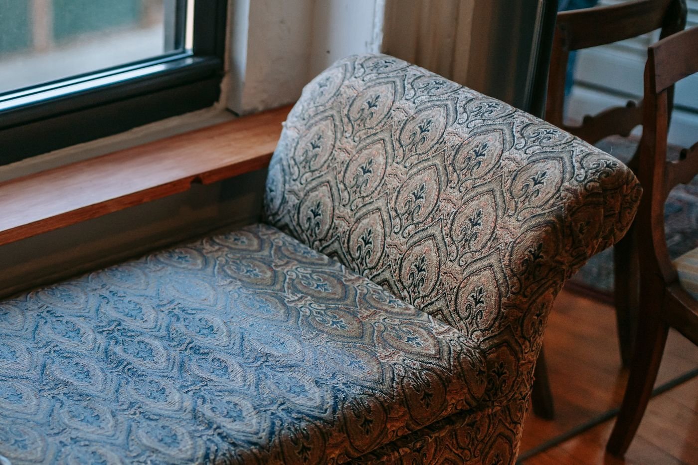 Representative photo of an antique bench with worn tapestry fabric by a window, ready for restoration