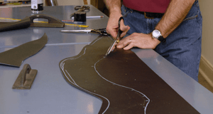 Upholsterer hand-cutting new material to a pattern for a reupholstery project at McCollum's Upholstery