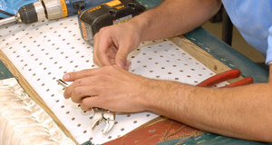 Hands rebuilding the base of a chair, fastening new webbing and springs to the frame at McCollum's Upholstery