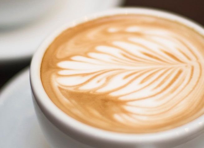 Latte with hand-poured leaf-pattern foam art in a white cup