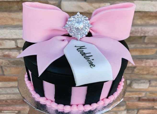 Custom cake styled as a pink and black striped gift box with a fondant bow and a name plaque