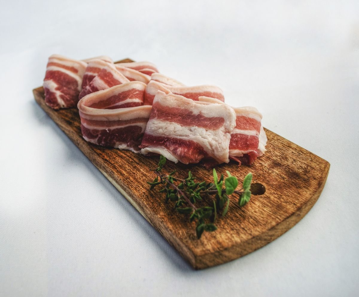 Representative photo: fresh-cut pork belly slices on a wooden board with herbs.