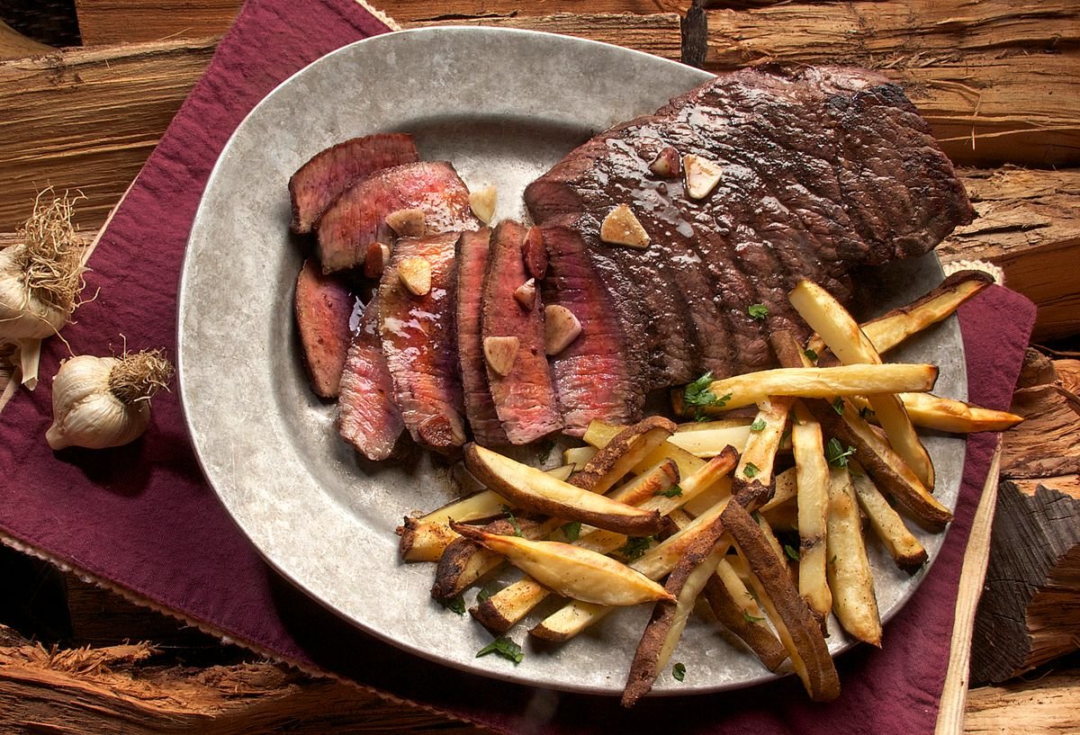 Representative photo: sliced grilled beef steak on a pewter plate with garlic and fries.