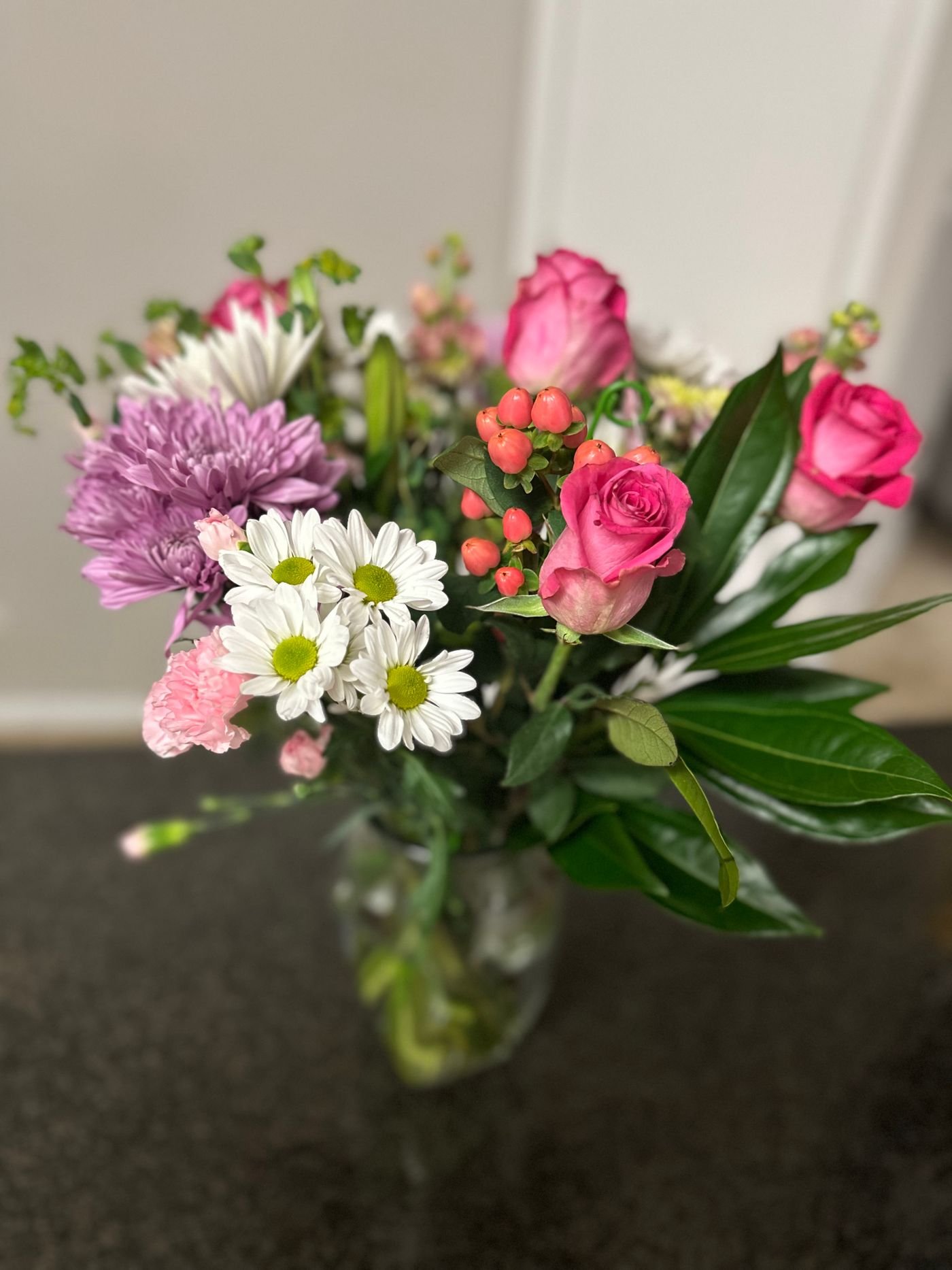 Representative photo of a colorful floral arrangement of roses and daisies in a vase.