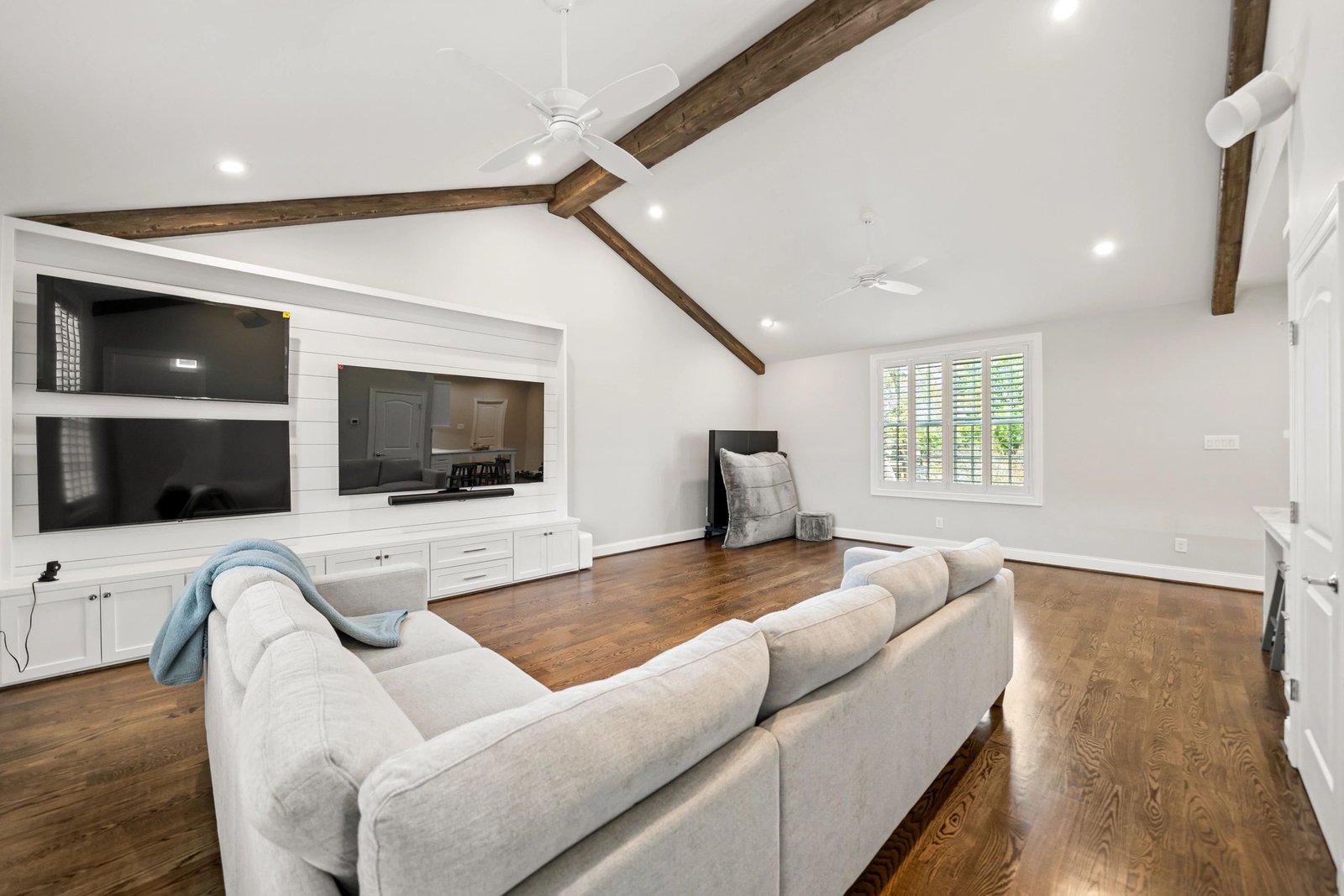 Vaulted living room with wood beams and built-in media wall by Olivo Remodeling