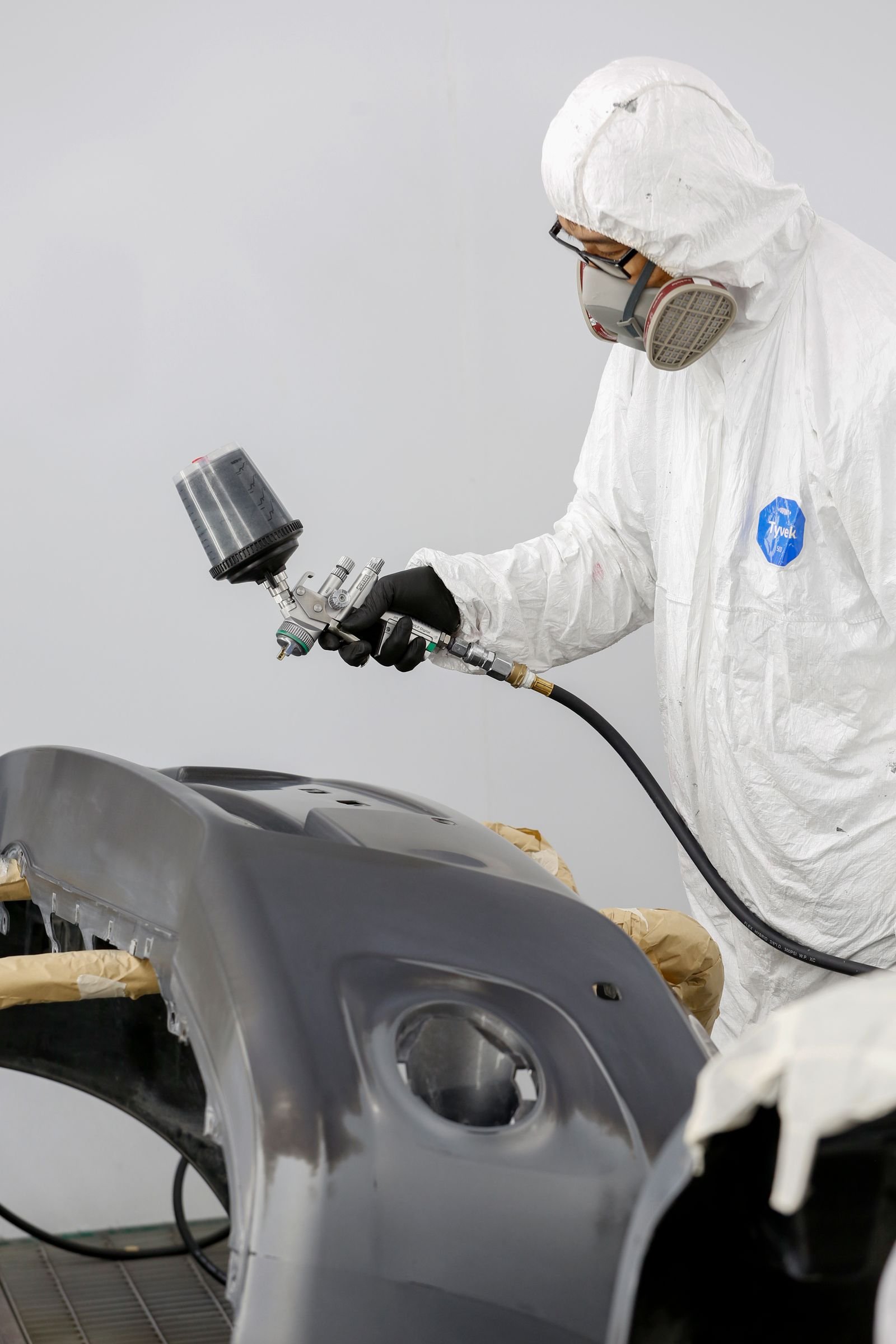Representative photo of a technician spray-painting a car panel in a professional paint booth