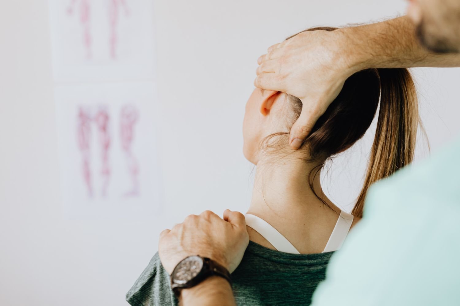 Representative photo of a chiropractor examining a patient's neck with spine and posture diagrams on the wall
