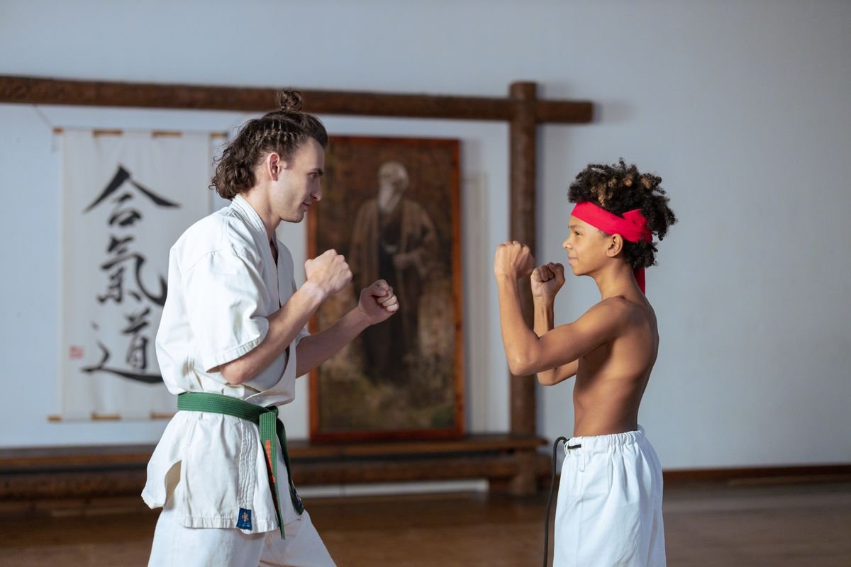 Representative photo of a karate instructor and a young student facing each other in fighting stances inside a dojo